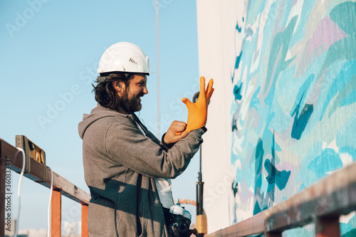 Contractor, artist at high altitude in a building cradle puts on gloves and prepares to carry out facade painting photo