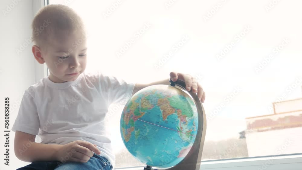 boy studies globe. education travel tourism concept. child twists the globe sits on a window sill. kid looking for a country on a globe map. world map geography lifestyle study boy studies globe. education travel tourism concept. child twists the globe sits on a window sill. kid looking for a country on a globe map. world map geography lifestyle study