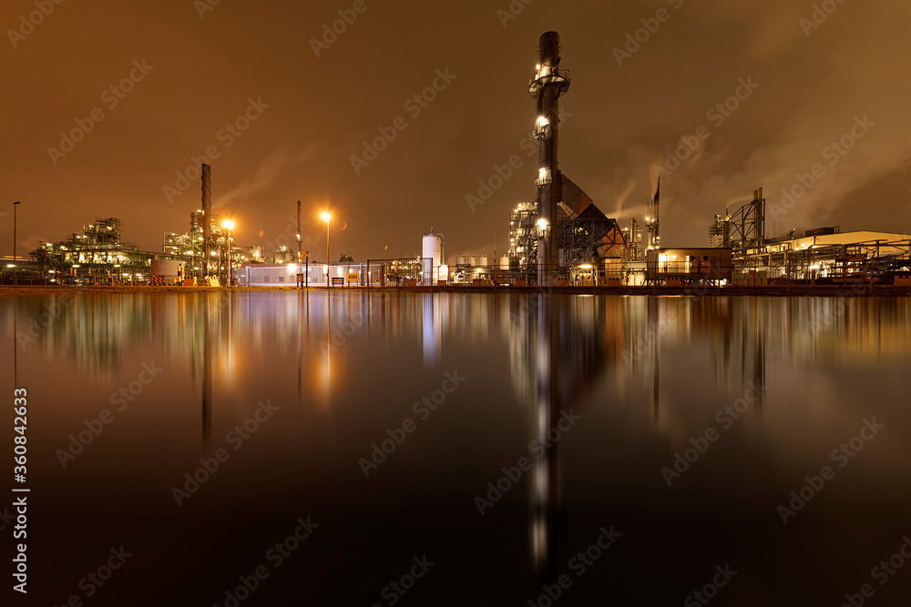 Refineries reflection and its chimney during the on fire sunset golden hour moment at Rotterdam, Netherlands
