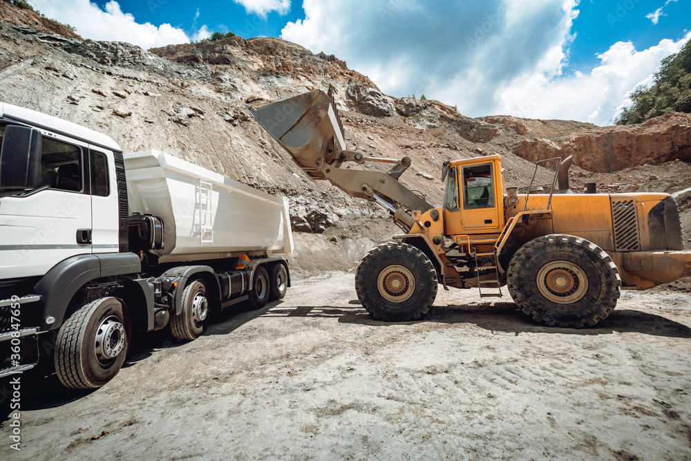 Industry details - machinery working. Wheel loader loading gravel into dumper trucks Industry details - machinery working. Wheel loader loading gravel into dumper trucks