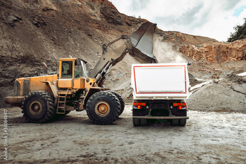 Industrial dumper trucks and wheel loader bulldozer working on highway construction site  loading and unloading gravel and earth materials. heavy duty machinery activity.