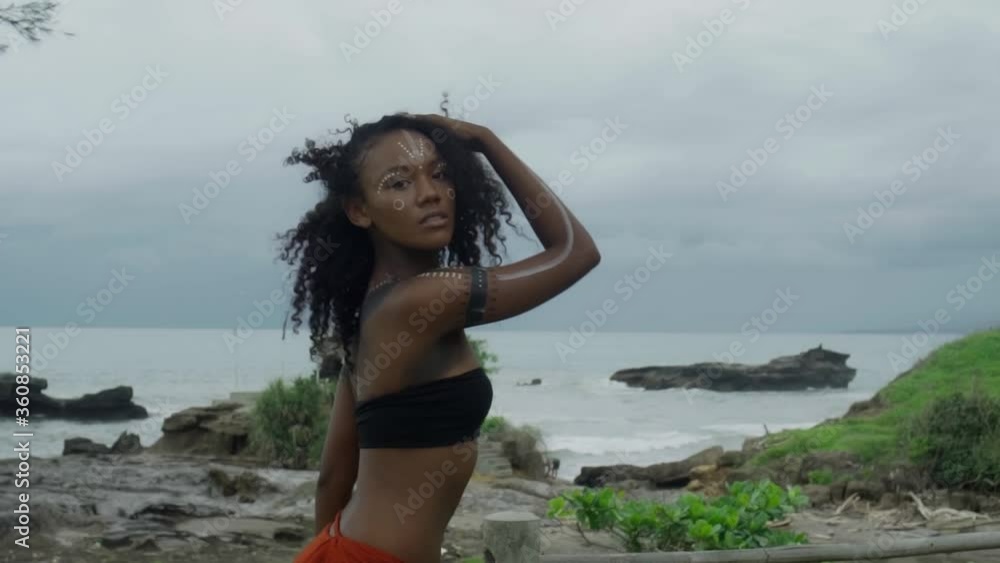 Africa girl with makeup and painted etnic lines on the body walking in a tropical garden