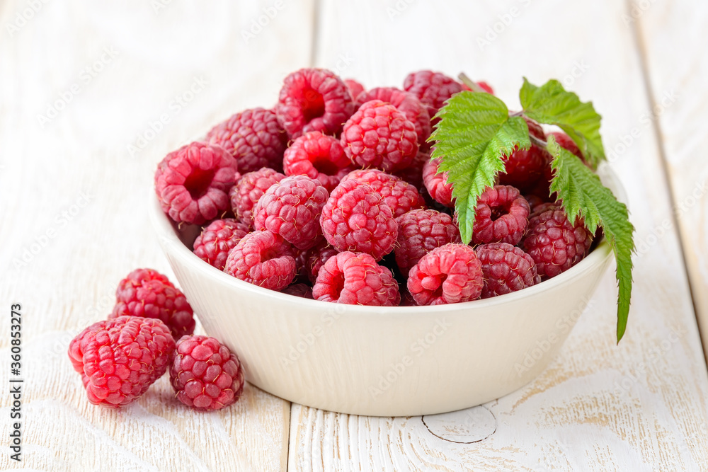 Whole ripe sweet raspberries and green leaf in a beige ceramic bowl on a white wood table. Tasty fresh organic fruits and berries, vegetarian and healthy eating. Raw food diet. Whole ripe sweet raspberries and green leaf in a beige ceramic bowl on a white wood table. Tasty fresh organic fruits and berries, vegetarian and healthy eating. Raw food diet.