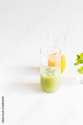 Two glasses with green and orange detox juices and ice cubes on light background. 