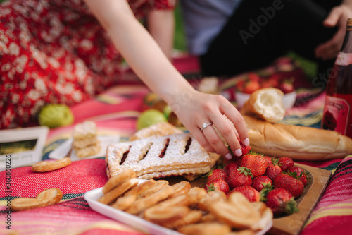 Close up of hand take strawberry on mini picnic outdoors. Man and woman eat outside