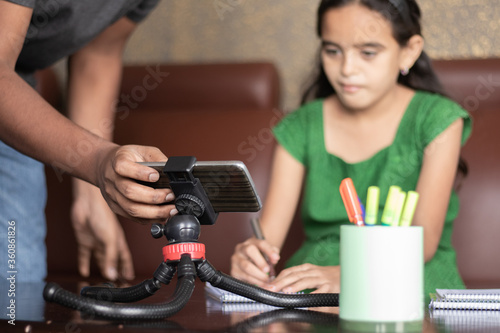Father helping daughter by adjusting mobile to studying the lesson of online class or e-learning - concept of Role of parent in supporting child during virtual class, homeschooling, distance learning.