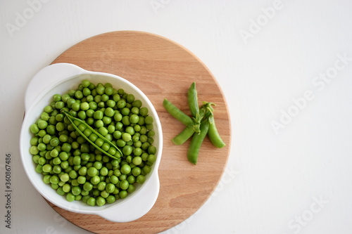 Fresh green peas and pods in white bowl on wooden cutting board. Healthy food  farm harvest concept.