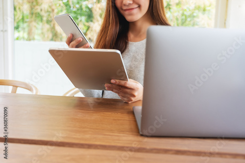 A young woman holding and using mobile  phone , tablet pc and laptop computer on wooden table