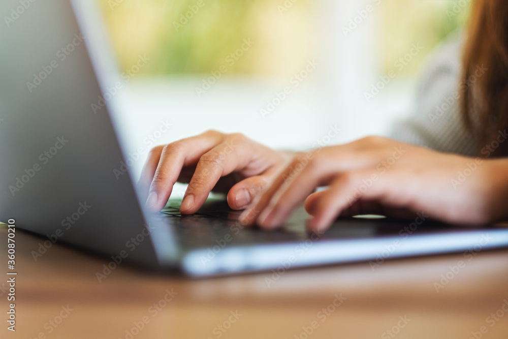 Fototapeta premium Closeup image of a young woman working and typing on laptop computer keyboard on wooden table