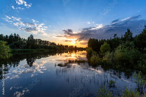 Beautiful summer sunset with clouds and reflection sun in water on the river.
