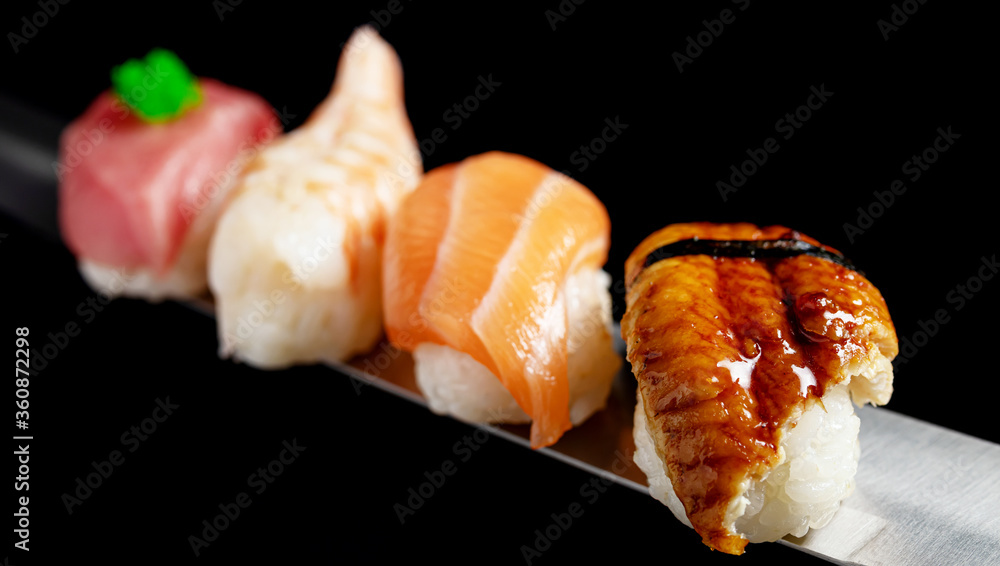 Japanese rolls and seafood sushi on a katana sword on a black background Japanese rolls and seafood sushi on a katana sword on a black background