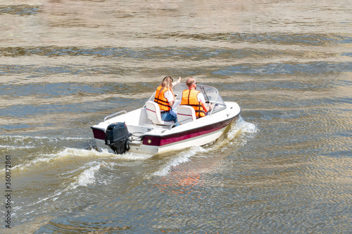 Young couple driving the speed boat in the river, wearing life vest. Shot at bright summer day. Nice tourist attraction to explore nature and the city.