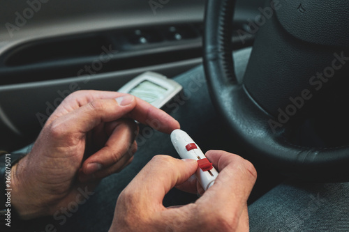 Diabetic man taking blood sample with lancet pen at car  closeup. Diabetes concept.