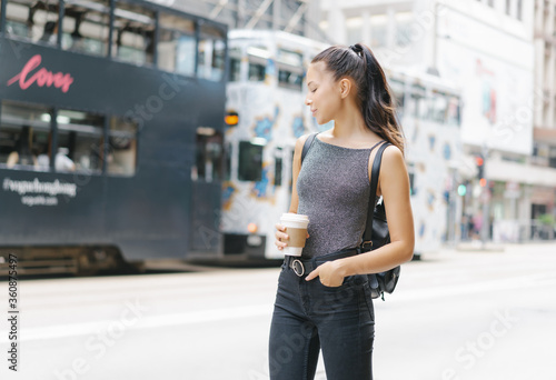Portrait of beautiful woman holding coffee cup of hot drink and enjoying the walk in the city, smiling enjoy weekends, travel with backpack.