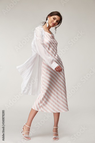 Sexy fashion model beautiful woman pretty face makeup, tanned skin wear summer collection clothes style for romantic date walk trendy light silk in white pink stripes long dress white shirt earrings.