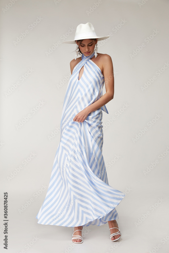 Sexy fashion model beautiful woman pretty face natural makeup tan skin body wear summer collection clothes style romantic date walk light silk in white blue stripes long dress earrings accessory hat. Sexy fashion model beautiful woman pretty face natural makeup tan skin body wear summer collection clothes style romantic date walk light silk in white blue stripes long dress earrings accessory hat.
