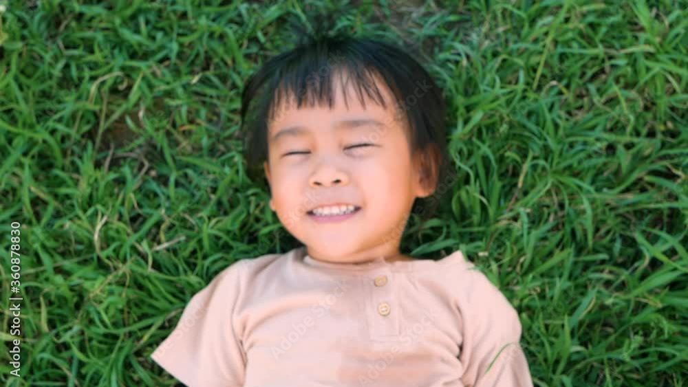 Happy little child girl lying on green grass outdoors in summer park. Happy little child girl lying on green grass outdoors in summer park.