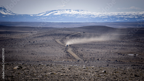 A lone car driving on the Kjalvegur mountain road through the central highlands of Iceland.
