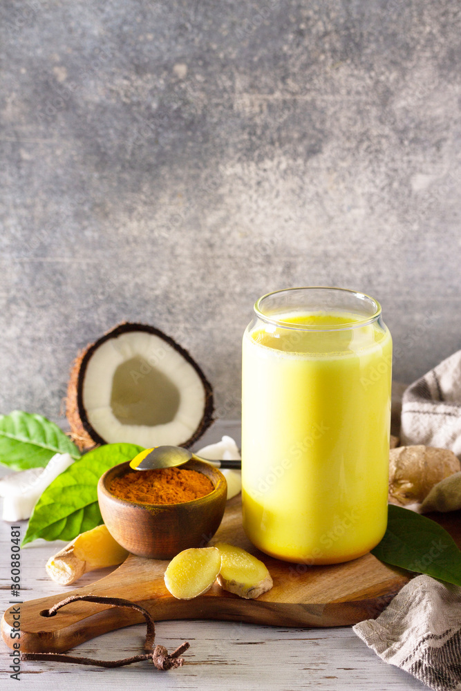 Cup of Healthy ayurvedic drink golden coconut milk turmeric iced latte with curcuma powder on kitchen table. Copy space. Cup of Healthy ayurvedic drink golden coconut milk turmeric iced latte with curcuma powder on kitchen table. Copy space.