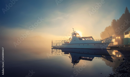 sea tourism. foggy morning on the lake, bright sun, ship and boat in backlight near the shore.