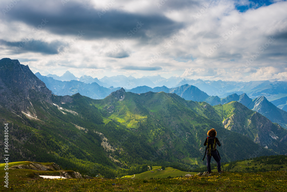 Woman with backpack resting on mountain top, looking at view dramatic landscape valley summer activity fitness wellbeing freedom concept, rear view