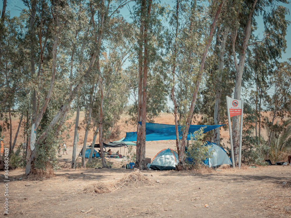 Many dome tents at a camping site near the Eucalyptus trees in Jordan Valley of Israel. Adventure vacation near the Jordan river on a sunny summer day. A sign symbolizing swimming is prohibited.