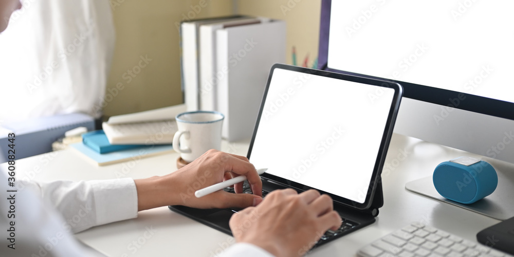 Cropped image of a businessman is using a white blank screen computer tablet at the white working desk. Cropped image of a businessman is using a white blank screen computer tablet at the white working desk.