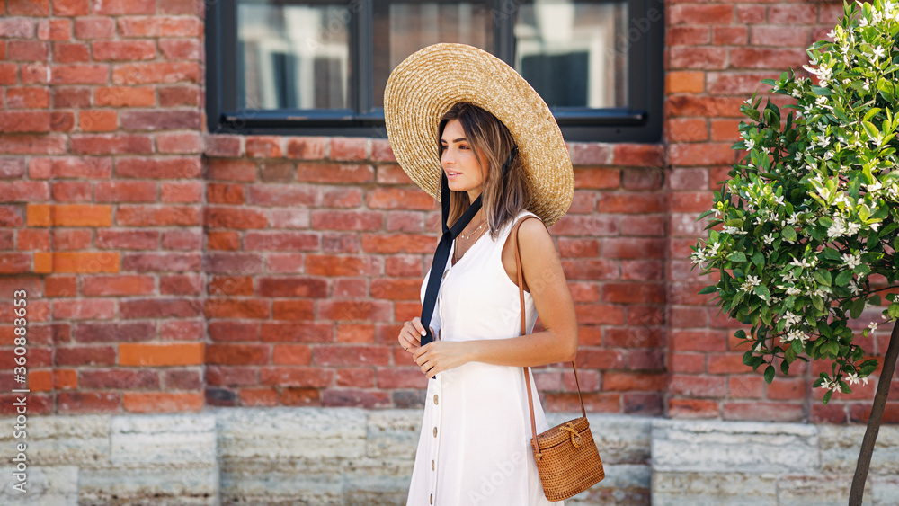 Stylish woman wearing straw hat walking on city street near a building