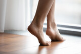 Crop close up of young woman barefoot step on warm wooden floor in bedroom or living room, female feet legs walk in room with underfloor electric heating at modern home or house