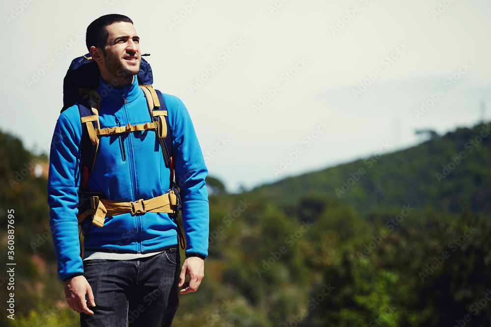 Portrait of a young tourist in mountain clothes and backpack standing on a top of mountain and enjoying scenery landscape view, hiker looking to copy space area for your text message or information Portrait of a young tourist in mountain clothes and backpack standing on a top of mountain and enjoying scenery landscape view, hiker looking to copy space area for your text message or information