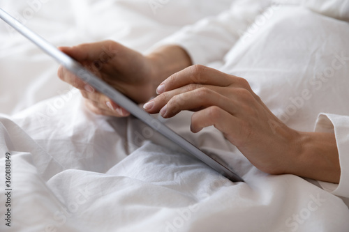 Crop close up of woman lying resting in bed using modern tablet gadget waking up in the morning, female awaken in home or hotel bedroom browsing Internet on pad device, technology concept