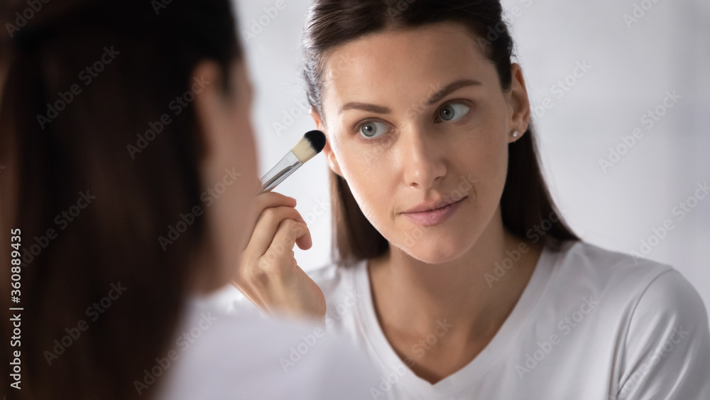 Beautiful millennial woman look in mirror do make up at home bathroom, pretty young brunette woman hold makeup brush get ready, perform daily beauty cosmetics procedure in bath in the morning Beautiful millennial woman look in mirror do make up at home bathroom, pretty young brunette woman hold makeup brush get ready, perform daily beauty cosmetics procedure in bath in the morning