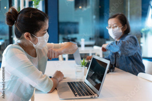 two asian woman are wearing face mask and making safe greeting by bumping elbow to say hi during covid-19 or coronavirus outbreak to prevent infection. social distancing and new normal concept