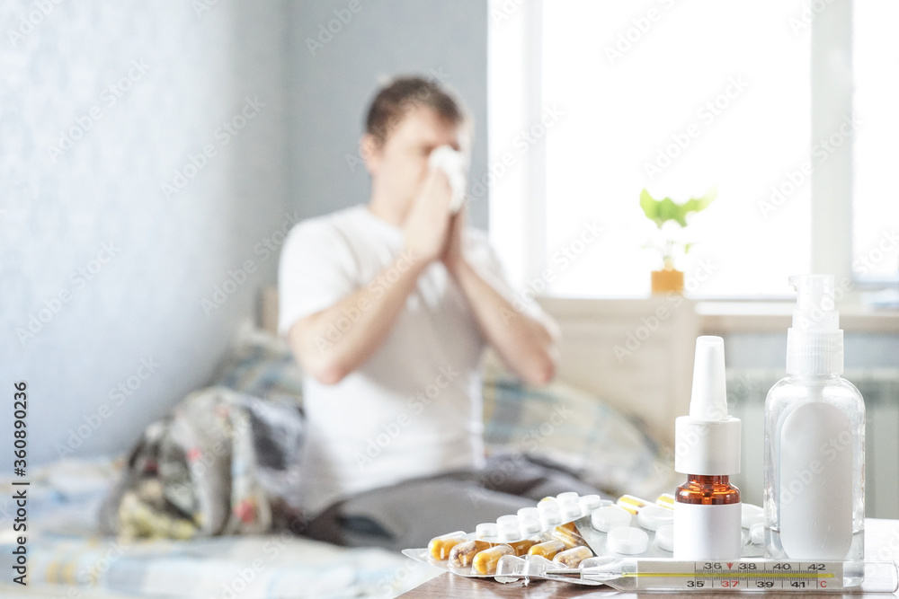 A sick guy is sitting at home on a sofa with a handkerchief and is taking medicine. Selective focus