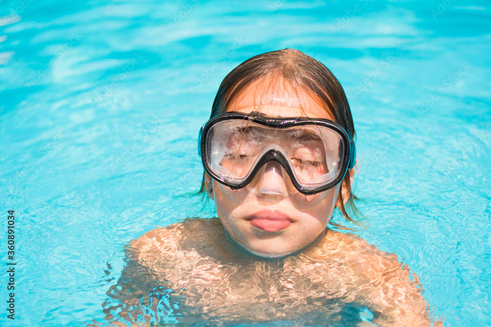 Pretty young girl in the water, portrait of kid with diving mask in swimming pool