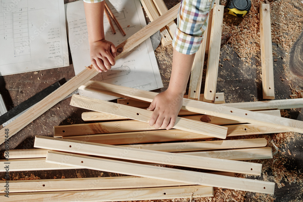 Above view of unrecognizable boy using sketches while assembling furniture in carpentry workshop Above view of unrecognizable boy using sketches while assembling furniture in carpentry workshop
