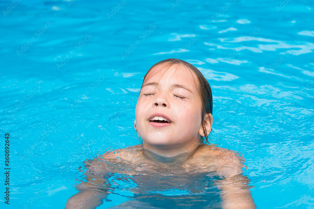 Pretty young girl is emerging from water, portrait of kid in swimming pool