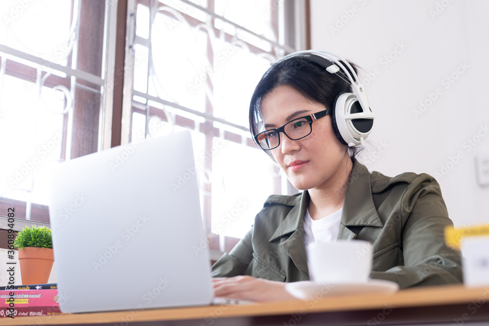 Modern young Asian woman working from home and listening to the music with a white headphones. Modern young Asian woman working from home and listening to the music with a white headphones.