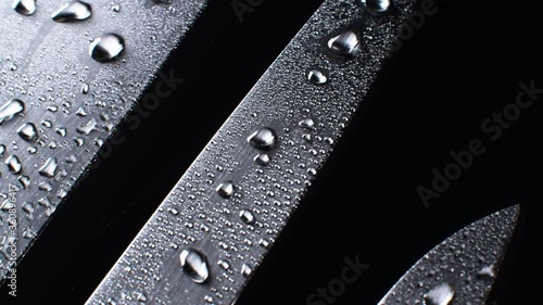 Extreme close up of three professional chef knives in water drops on black background. Macro shooting with motion control system. Smooth camera movement, top view