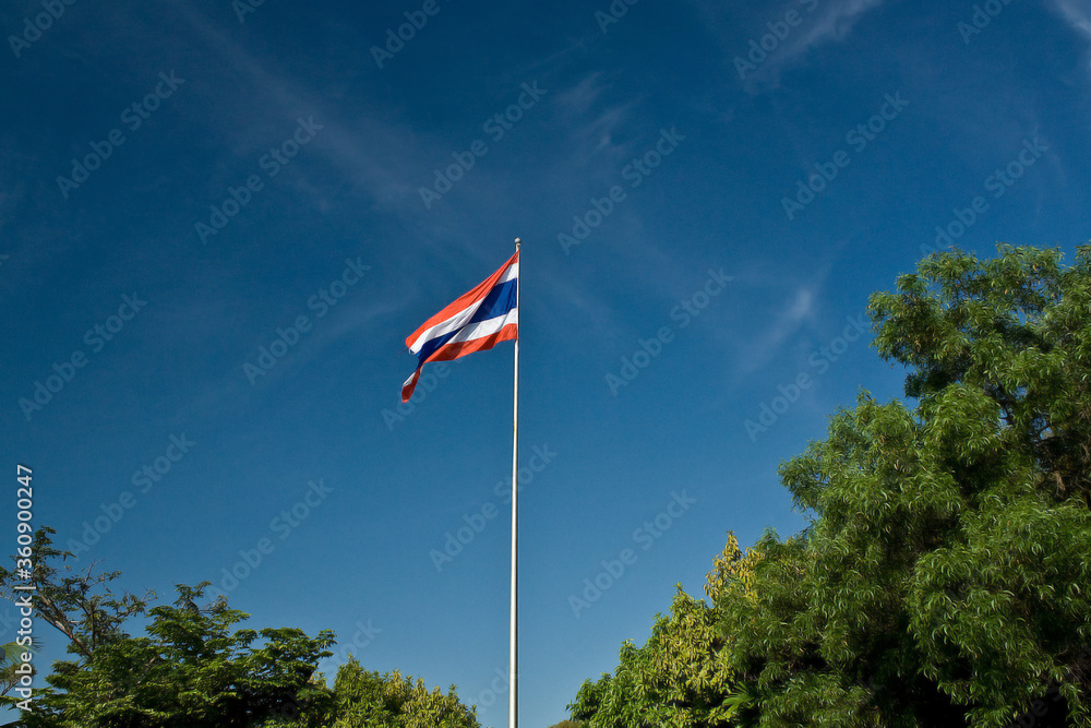 Image of waving Thai flag of Thailand with blue sky background and nature green