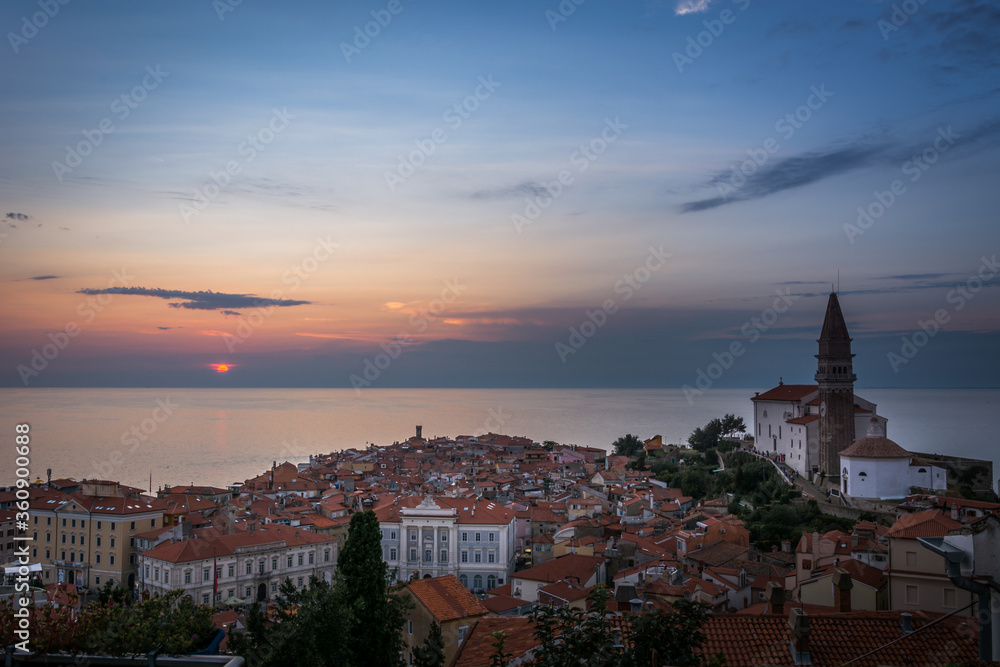 Famous church landmark in Piran town looking at sea during sunset golden hour in Slovenia. Summertime at the sea. Reflection of sun on surface