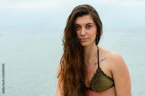 Young woman in bikini by the sea, portrait of a sexy girl on the beach, portrait of a dark-haired girl with sensual attitudes on the beach with green costume photo