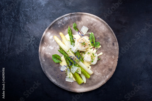 Traditional barbecue scallops with green and white asparagus and sauce hollandaise offered as top view on a rustic modern design plate with copy space