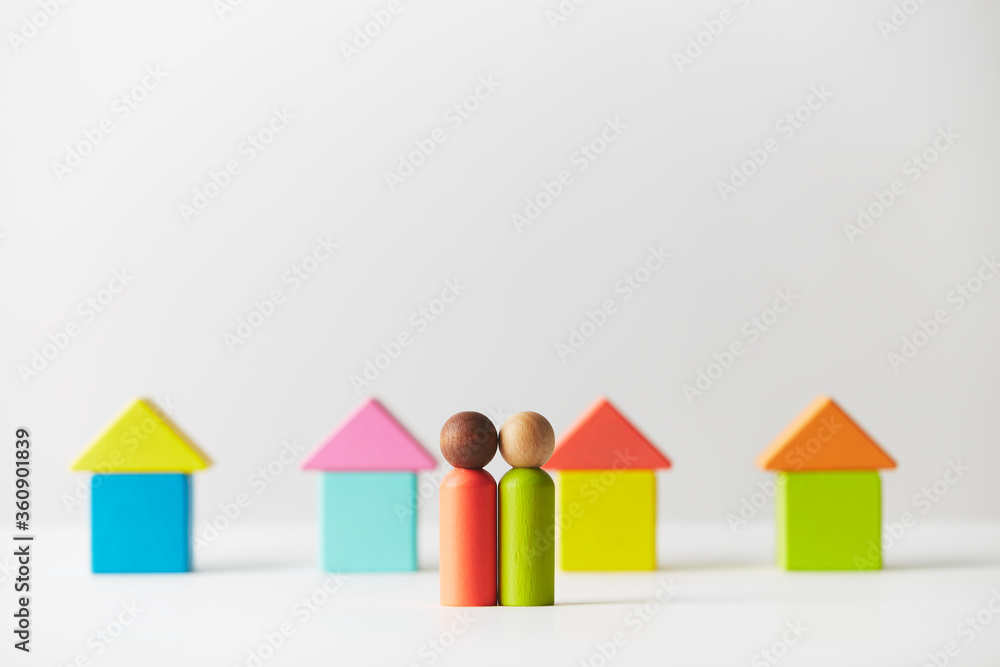 Wooden figurines concept. Two wooden figures people standing in front of a line of block houses, mixed skin colour. Realty market of Residential Development. Kids toys