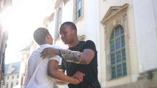 Two black men met in the middle of the street. They shake hands and hug. Sun glare portrait. Students near the university
