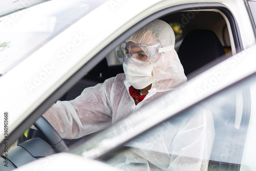 man sits in a car in a protective suit, goggles and a medical mask for respiratory protection