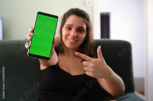 Young caucasian woman pointing at her smartphone with green screen