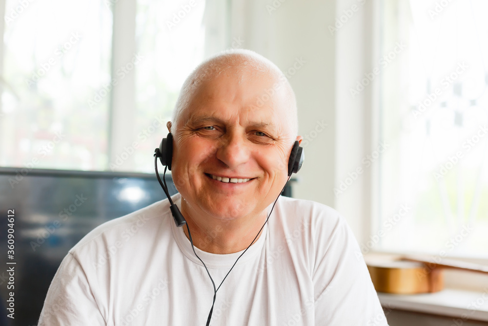 Elderly man with headphones and computer laughing happily, telework, e-business or commerce, customer support representative, video-chat, copy space Elderly man with headphones and computer laughing happily, telework, e-business or commerce, customer support representative, video-chat, copy space
