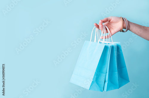 woman hand carrying a bunch of blue shopping bags over blue background