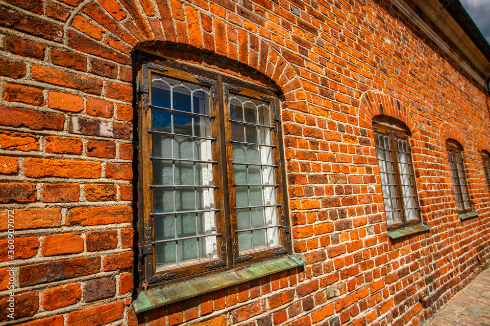 an old industrial wall made of red brick stones with  windows made of glass and lattice